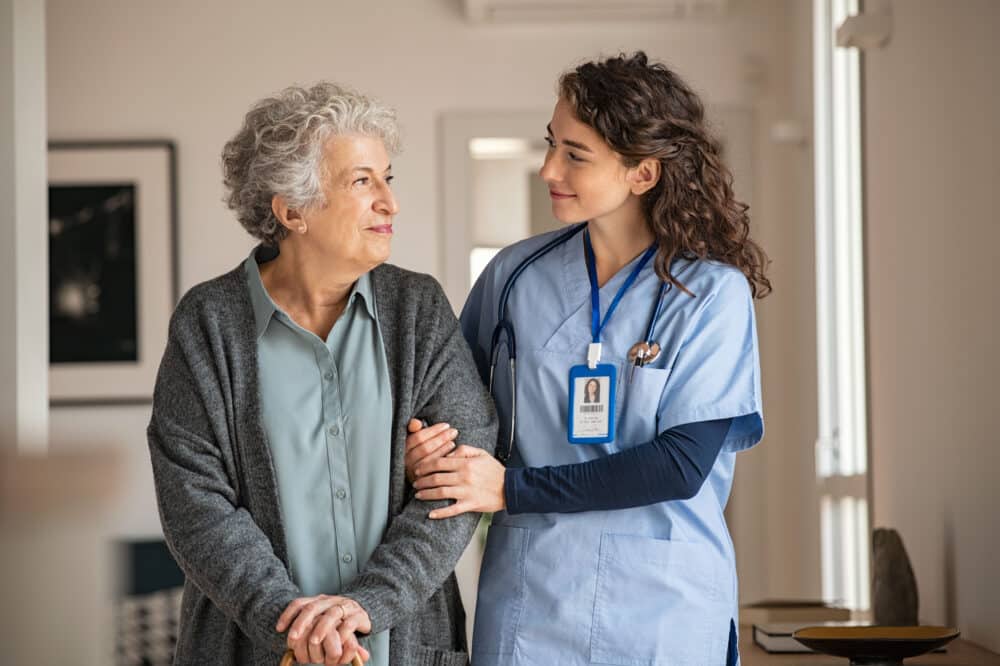 Young caregiver helping senior woman walking. Nurse assisting her old woman patient. Senior woman with walking stick being helped by a nurse.