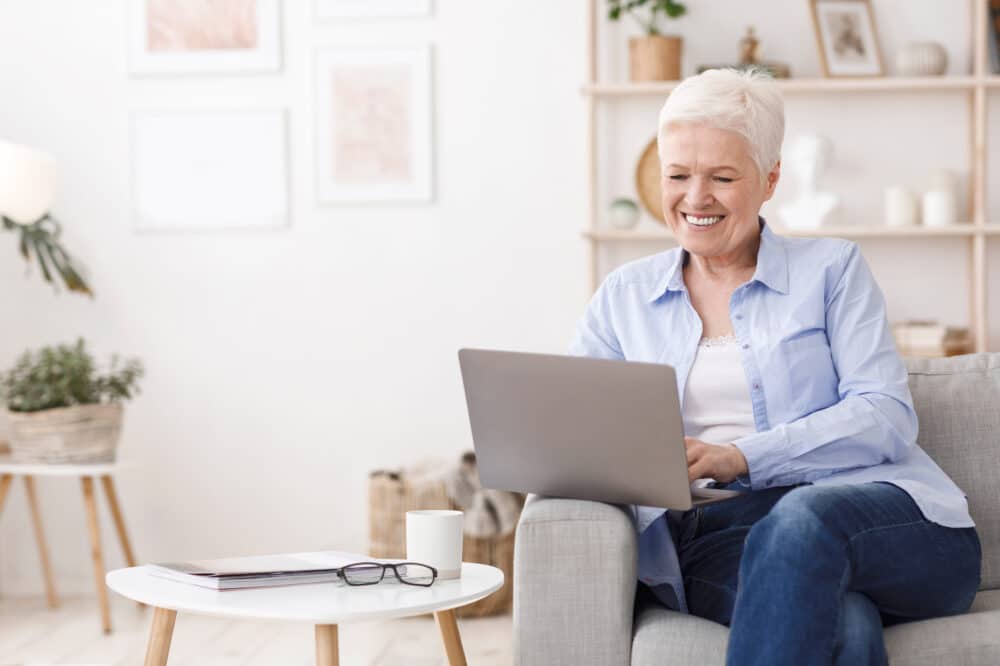 Happy Elderly Woman Study With Laptop At Home, Sitting On Sofa In Living Room