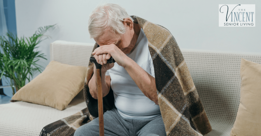 Elderly man wrapped in a plaid blanket leaning on a cane, appearing tired and contemplative while sitting on a couch, highlighting the importance of compassionate memory care for elderly individuals.