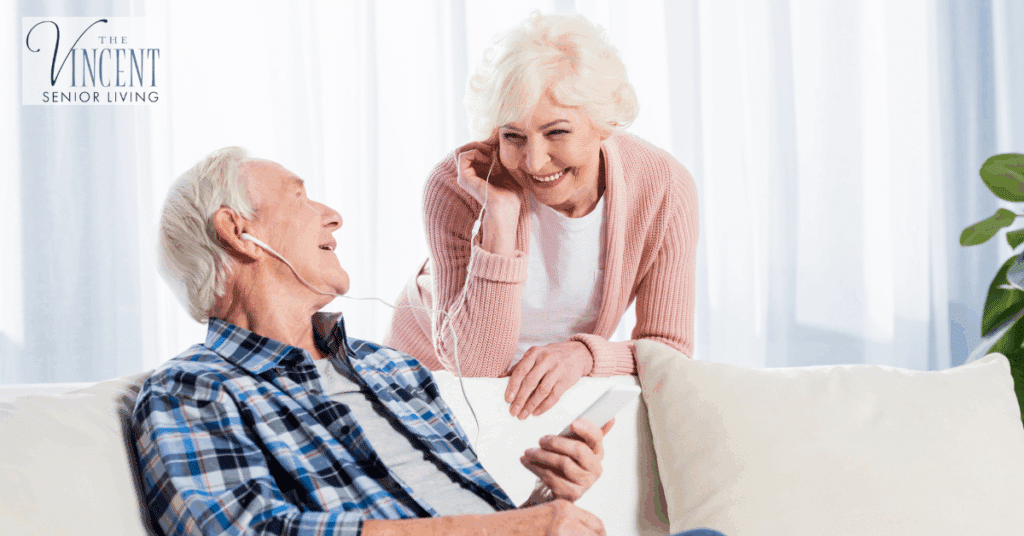 Visiting a loved one in memory care — a cheerful senior couple sitting together, sharing earphones and smiling while listening to music.