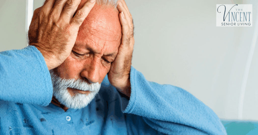 An older man holding his head with both hands and appearing distressed, representing dementia anger and other challenges often addressed through senior memory care services.