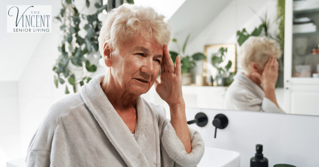 Older woman in a bathroom touching her head, showing how daily dementia hygiene routines may need gentle support.