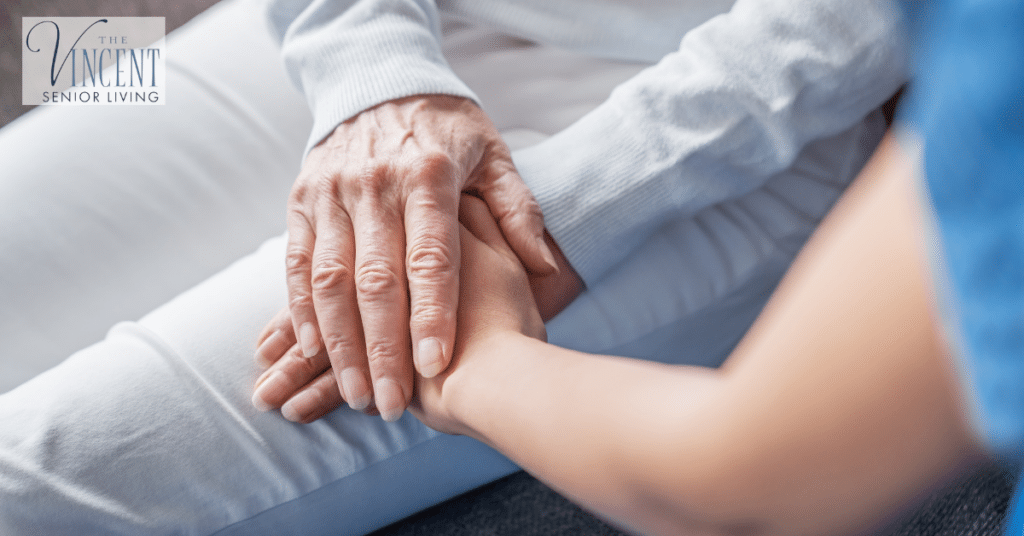 Care partner holding an older adult’s hand to provide comfort and reassurance during the transition to memory care.