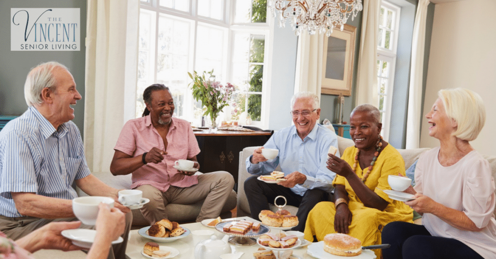 Seniors enjoying tea and pastries together in a bright living room, highlighting social connections and companionship while living with Alzheimer's and dementia.
